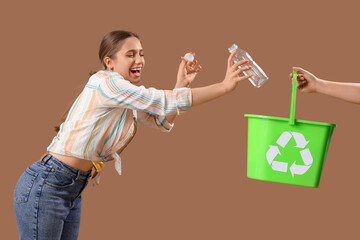 Young woman throwing plastic bottle into recycle bin on brown background. Waste sorting concept