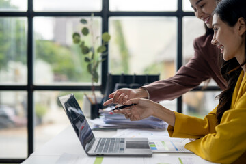 Two women are sitting at a desk with a laptop open