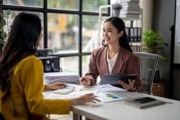 Two women are sitting at a desk, one of them holding a tablet