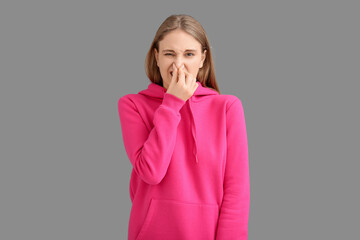 Young woman  pinching nose because of bad smell on grey background
