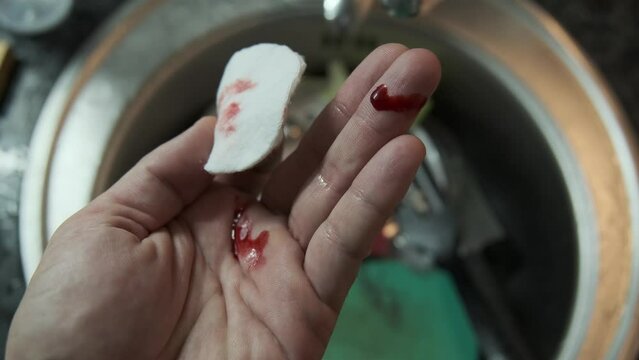 Close-up of a hand with cut finger being treated with a cotton pad to stop the bleeding while washing dishes, highlighting first aid care in everyday kitchen accidents