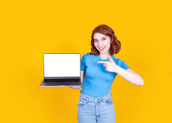 Laptop mock up, smiling young caucasian woman holding laptop mock up. Pointing index finger on pc computer blank empty screen standing over yellow studio background. People lifestyle concept idea.
