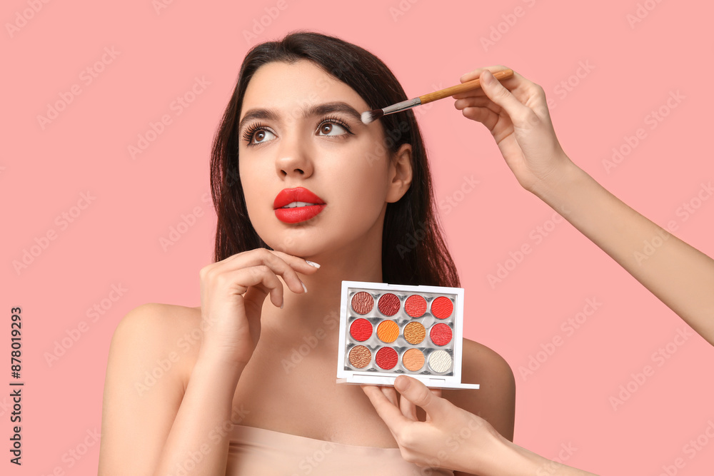 Poster Female makeup artist working with young woman on pink background