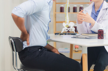 An orthopedic doctor shows a spinal model to a patient in a human spinal hospital. Diseases and...