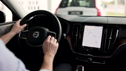Customer experiences vehicle features exploring driving comfort and technology. Businessman drives new car inside dealership featuring modern navigation system. Car purchase, lease discussion likely.