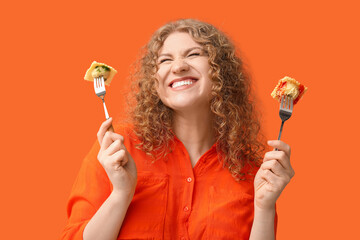 Happy young woman holding forks with tasty ravioli on orange background