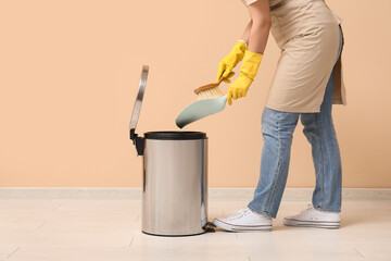 Woman sweeping dust off dustpan into trash bin on beige background