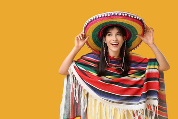 Young woman in sombrero and colorful poncho on yellow background. Cinco de Mayo celebration
