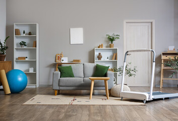 Interior of light living room with treadmill and sofa