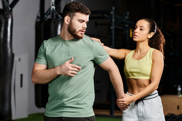 Fototapeta premium A male trainer is instructing a woman on self-defense techniques in a gym setting, focused and determined.