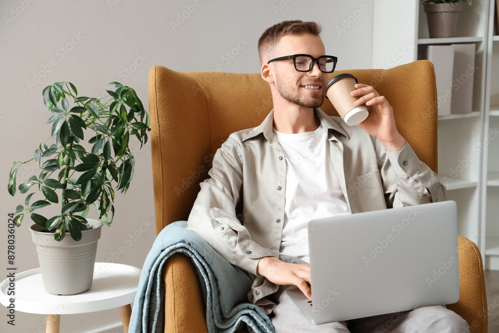 Canvas Prints Young bearded man in eyeglasses with laptop drinking coffee at home