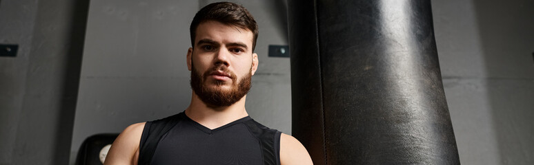 Obraz premium A handsome man with a beard boxing next to a punching bag in a gym.