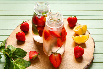 Sports bottles of infused water with strawberries, lemon and mint on green wooden background
