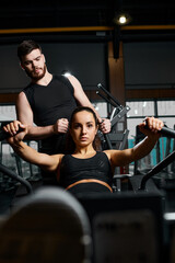 A male trainer is assisting a brunette sportswoman with exercises in a gym.