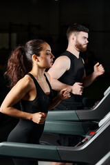 A personal trainer and a brunette sportswoman running on treadmills in a gym, keeping pace and...