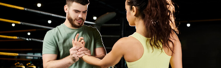 A male trainer demonstrates self-defense techniques to a woman in a gym setting.