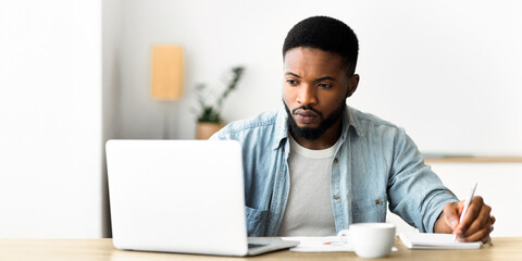 Job search. Unemployed man using laptop searching for vacancies online in internet and taking notes, panorama with copy space