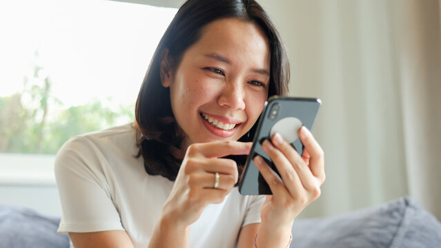 close up young asian woman hold smartphone and looking on device screen for check notification or read news or alert from application in living room at home for people lifestyle and technology concept