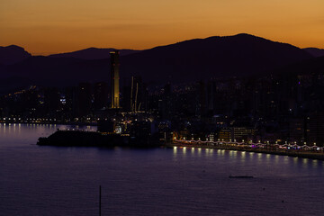 Fototapeta premium Night time aerial photo of Benidorm Playa Levante beach in the evening showing the sun setting behind the mountains and the hotels and high rise apartments on the beach front