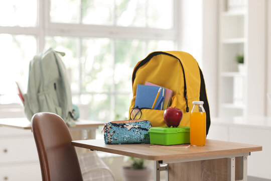 Apple with lunchbox, pencil case and backpack on desk in classroom