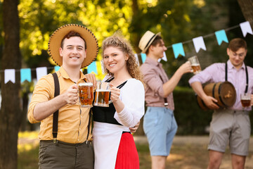 Young couple in traditional German clothes with beer celebrating Octoberfest outdoors