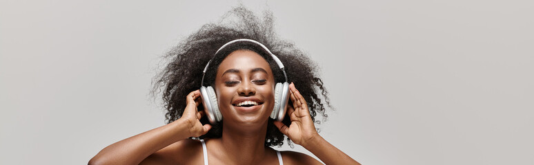 A young African American woman with curly hair wearing headphones, lost in the music shes listening to.