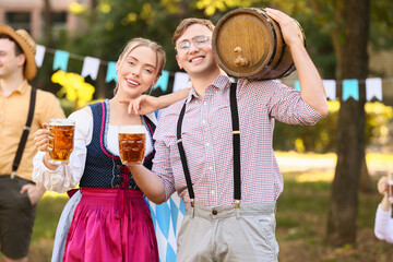 Fototapeta premium Young couple in traditional German clothes with barrel of beer celebrating Octoberfest outdoors