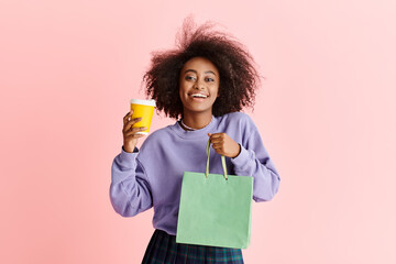 A stylish African American woman with curly hair holding a cup and a paper bag in a studio setting.