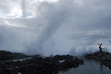 Fishermen stand defiant against a massive wave, arms outstretched, as the tumultuous sea meets a...