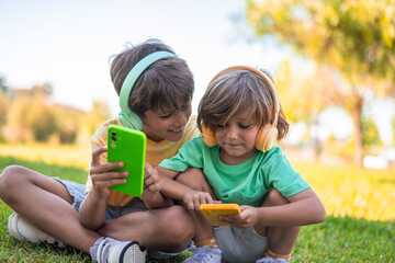 Children Enjoying Music and Games on Smartphones. Happy children with headphones and smartphones in the park.