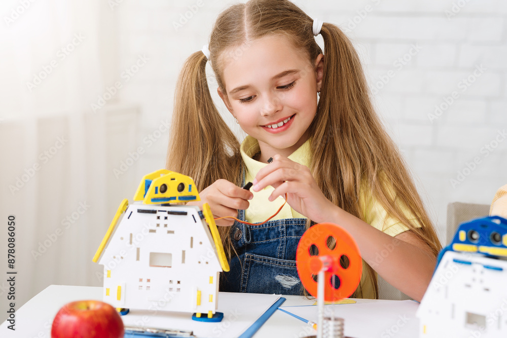 Poster a young girl with pigtails is sitting at a table, intently building a robot toy. she is connecting w