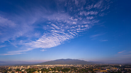 Obraz premium Expansive view of a city under a clear blue sky with scattered clouds and a mountainous backdrop.