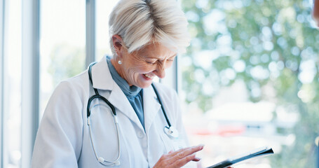 Mature woman, doctor and laughing with tablet for telehealth, medical research or meme at hospital. Senior, female person or healthcare employee with smile on technology by window for communication
