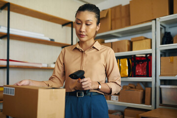 Asian young woman scanning code of order with scanner while working in warehouse