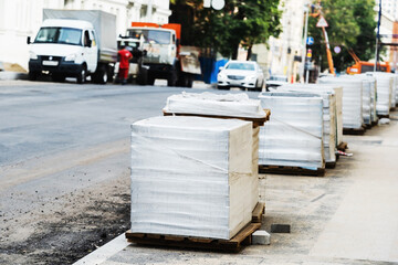 Obraz premium Paving stones in packages delivered by a building materials supplier. Construction and repair of pedestrian paths on a city street. Foreground. Selective Focus