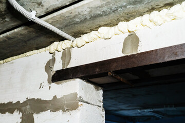 A close-up of a concrete beam sealed with expanding foam and mortar in a basement