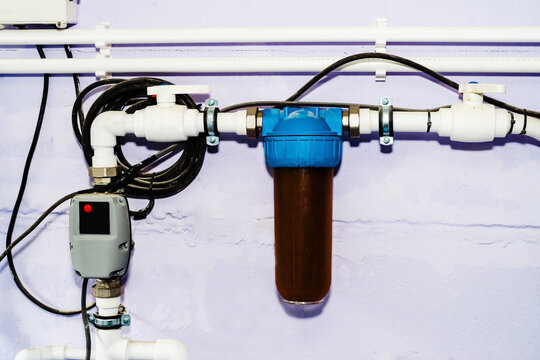 A close-up shot of a water filter system attached to a white wall. The filter is blue and white and has a brown filter cartridge