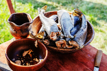 Smoked fish in a clay bowl on a wooden table, with a clay jug and knife