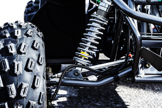 A close up of a black off road vehicles suspension system. The image shows the large tire, a shock absorber, and part of the frame