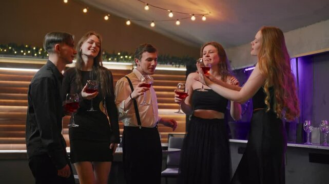 Young people celebrating Christmas, dancing in nightclub and drinking red wine. Merry party of best friends in winter holidays, Xmas and New year festival, cheerful women and men have fun and joy