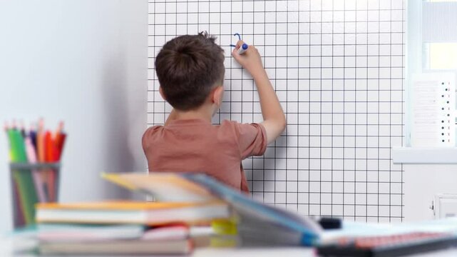 Rear view of young boy solving math problems on white board