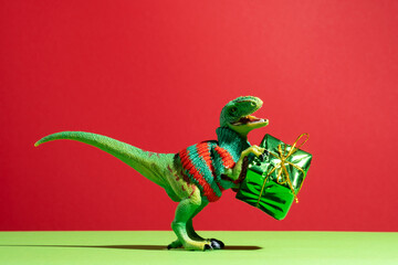 Cute dinosaur in knitted sweater with present box on red and green background.