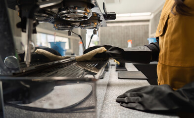 Female Employee Cleaning Coffee Shop Espresso Machine with Gloves in Modern Cafe Setting