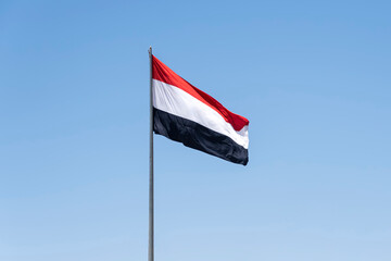 Flag on Yemen flag pole and blue sky, Flag of Yemen fluttering in blue sky national symbol. Waving white Yemen flag, Independence Constitution Day.