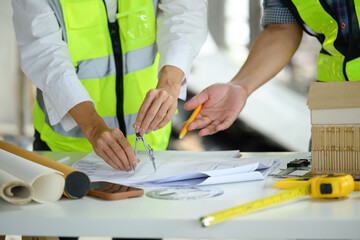 Architects reviewing blueprints and notes on a table at construction site with laptop and architectural model