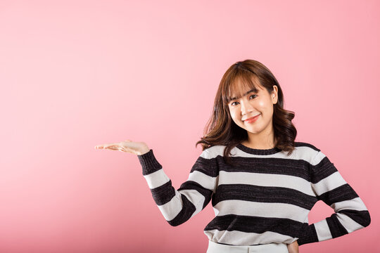 Asian happy portrait beautiful cute young woman smile standing presenting product holding something on palm away side, studio shot isolated on pink background with copy space, female show hand gesture