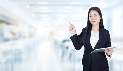 An Asian woman in professional attire, smiling and holding up one finger while pointing other side