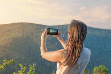 A woman uses her smartphone to capture a scenic view of mountains and enjoy the peaceful outdoors