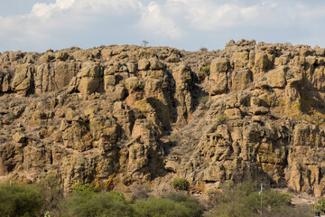 Impressive Rocky Cliff Formation Under a Partly Cloudy Sky with Verdant Vegetation Below