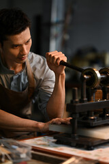 Professional male artisan in apron working with iron press machine in leather workshop